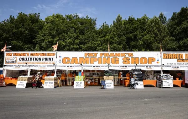 The Fat Frank's Camping Shop stall head on: a long white marquee with the shop name in orange across the front, the collection point at the left-hand end and airbeds advertised at the right.